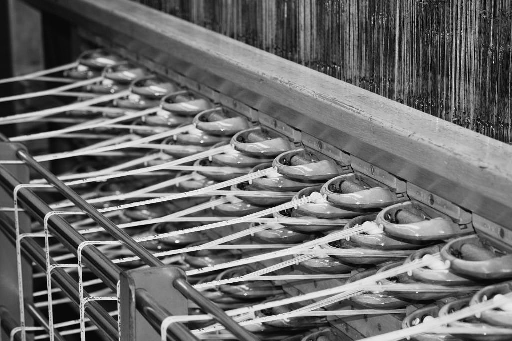 Quality First - Jacquard loom with multiple spools of cotton threads in an industrial weaving process.